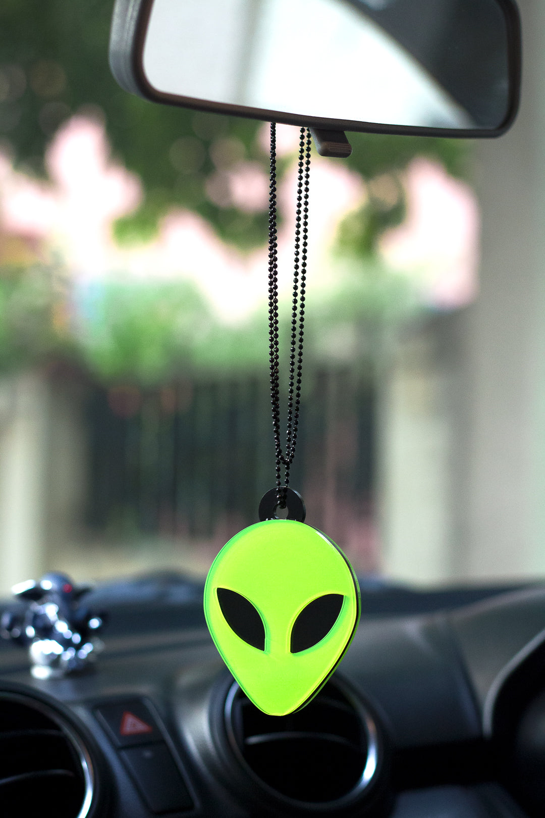 Green alien-shaped car air freshener hanging from a car's rearview mirror.