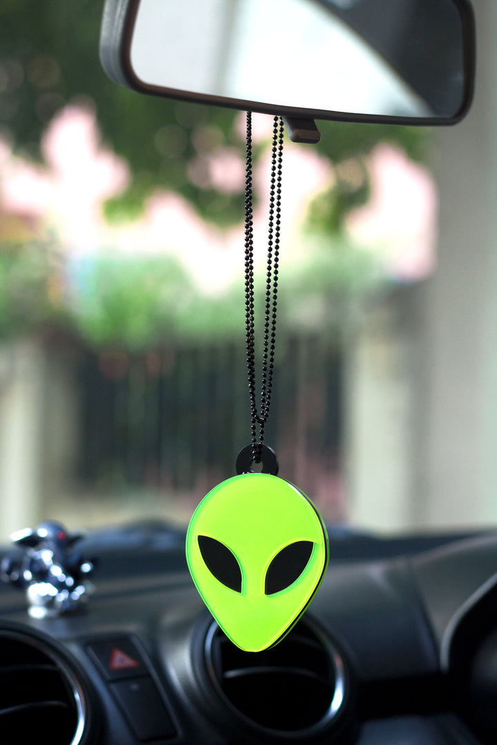 Green alien-shaped car air freshener hanging from a car's rearview mirror.