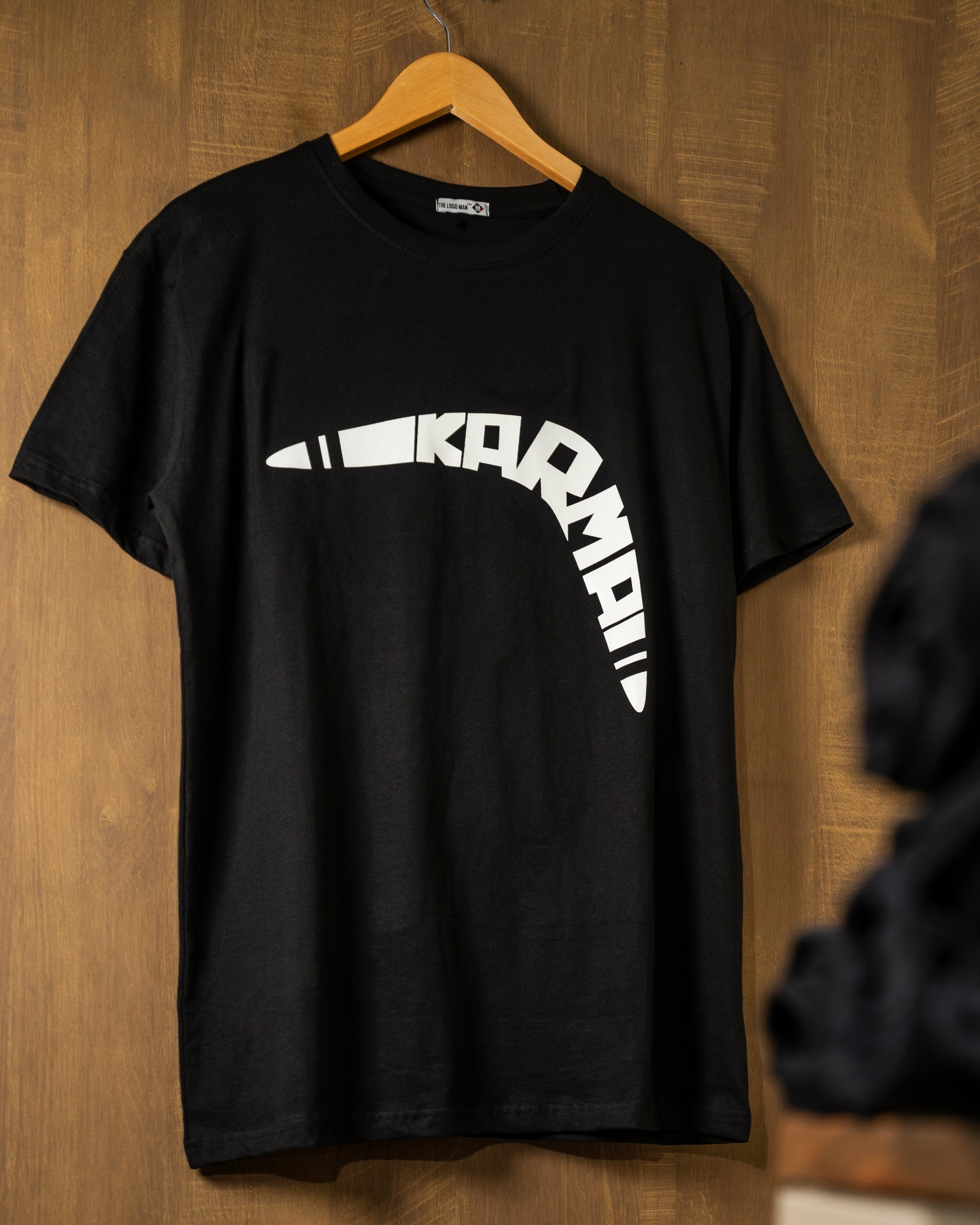 Black t-shirt with a white logo on a wooden hanger against a wooden wall.