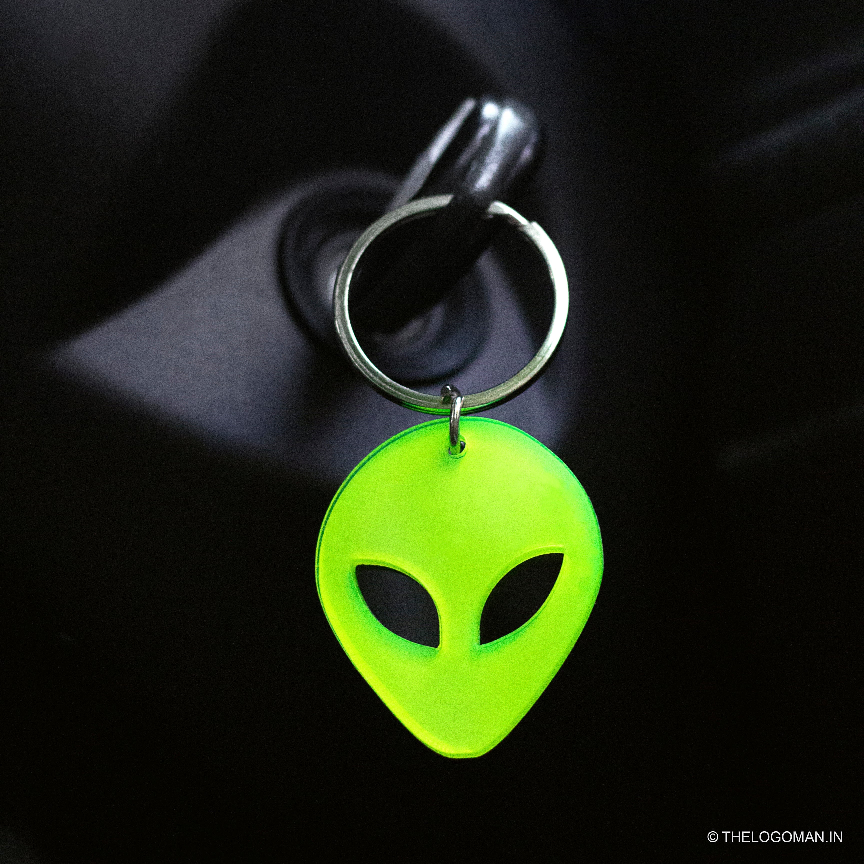 Green alien keychain on a car dashboard with a blue light in the background