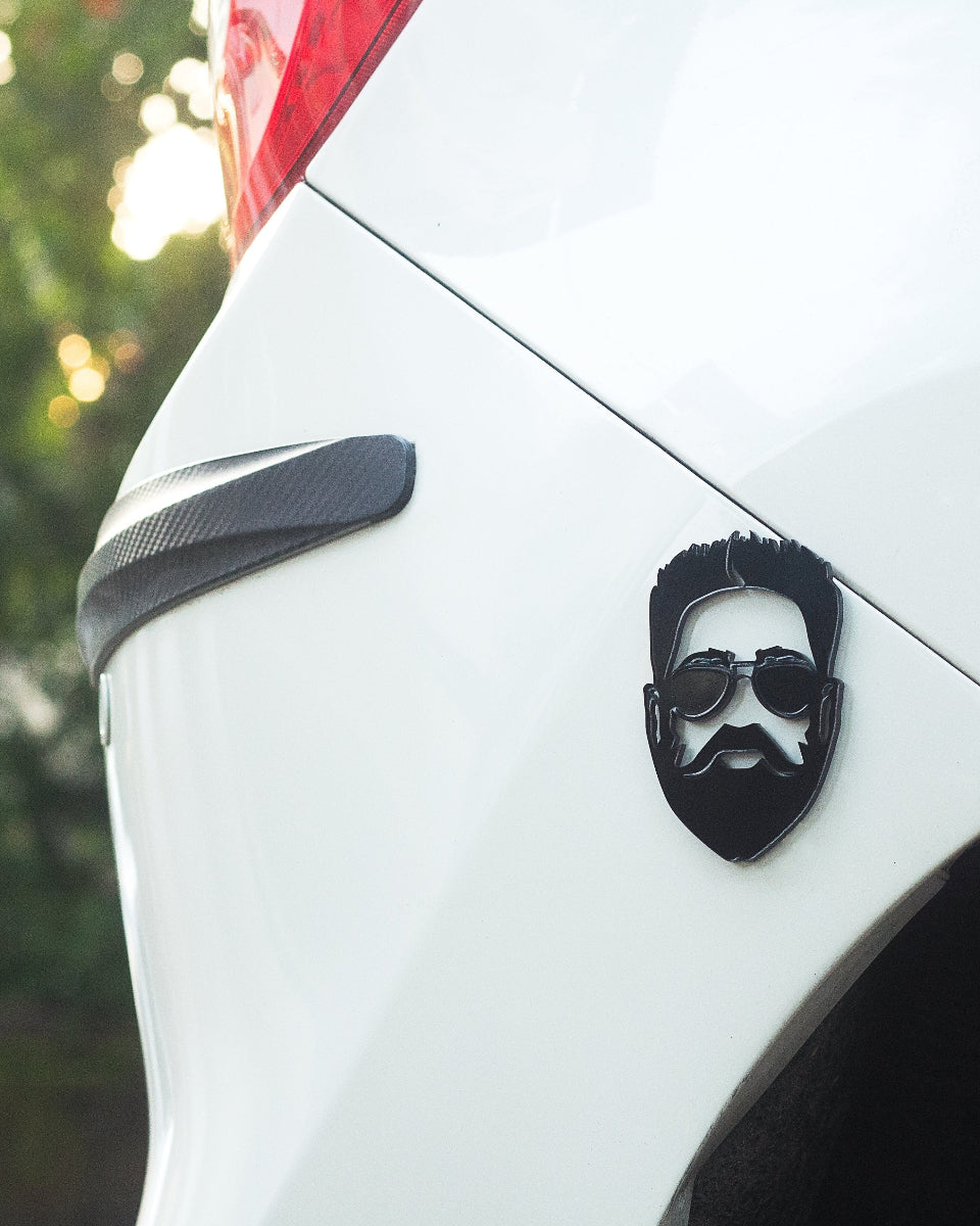 Car with a decorative emblem of a bearded man wearing sunglasses on the trunk.